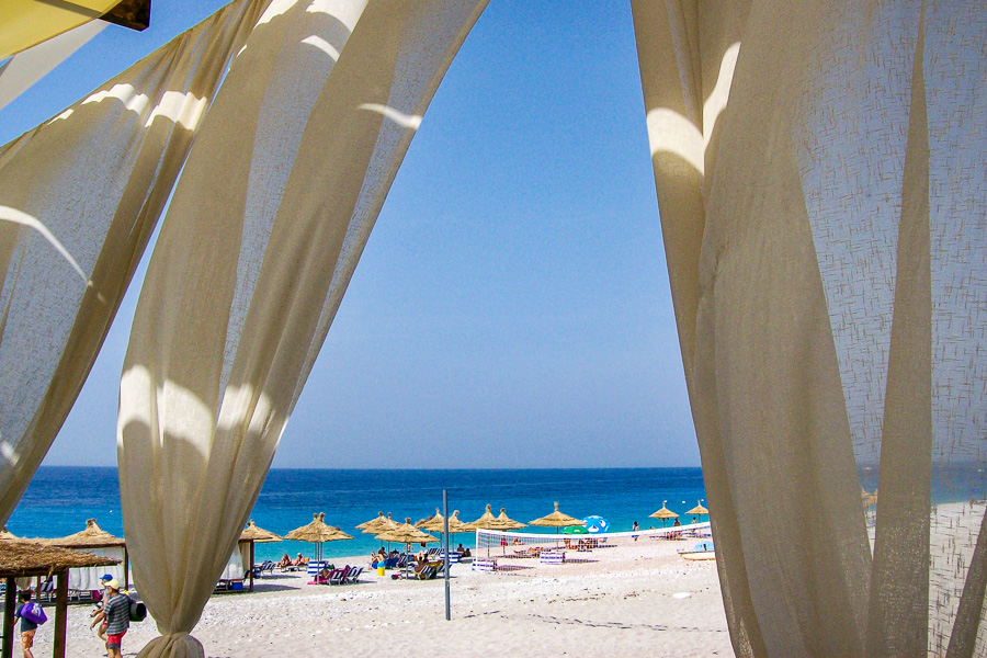 Sunny Ionian Coast beach in Albania, with straw umbrellas and turquoise sea