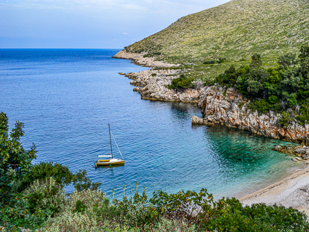 Sailboat next to a quite rocky beach in a turquoise bay on the Albanian Riviera Ionian Coast.