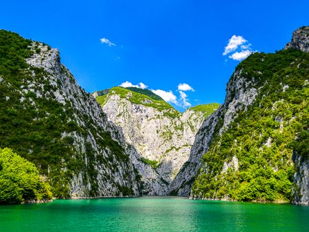 Turquoise waters of Koman Lake framed by steep green cliffs, northern Albania.